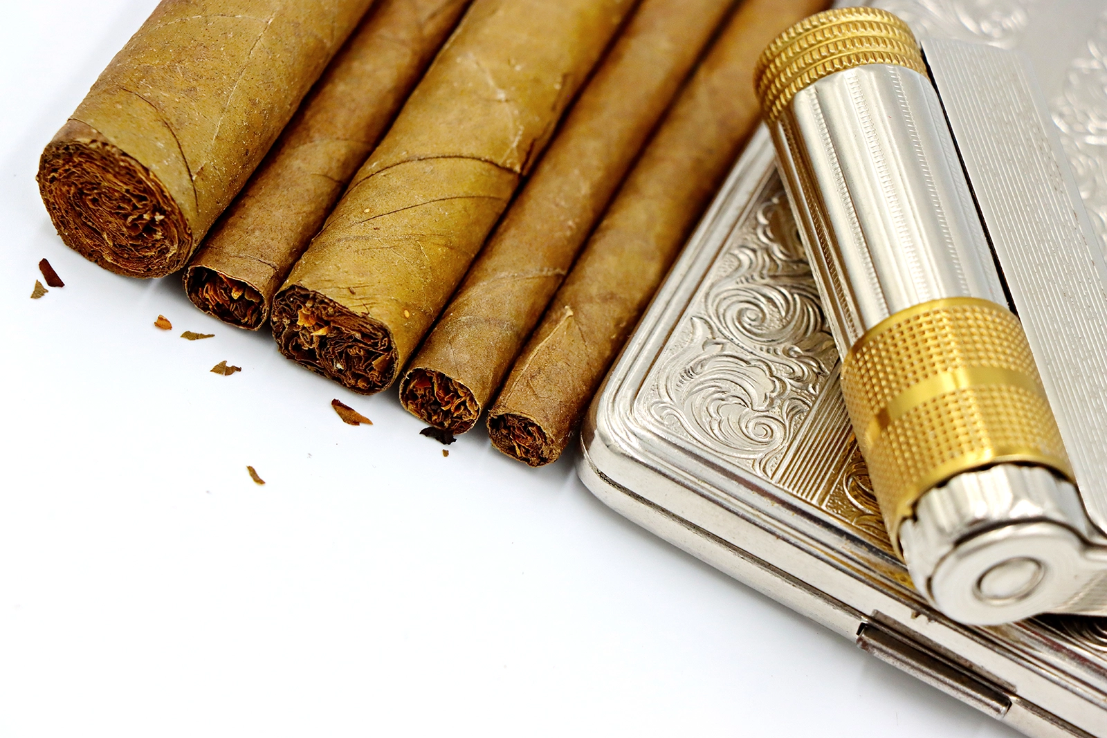 A set of various size cigars laid next to a stylish cigar case and a stylish metal lighter, all on white background.